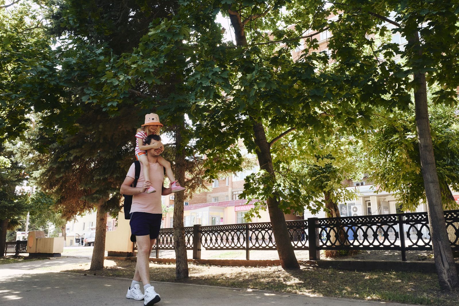 Тато несе доньку на плечах під час вечірньої прогулянки парком