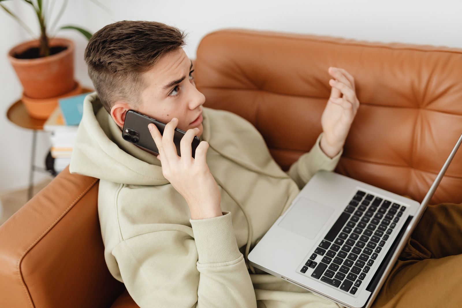 Підліток на дивані одночасно тримає смартфон і працює з ноутбуком