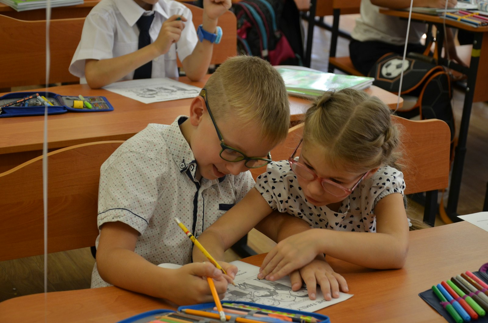 Двоє школярів разом малюють за партою в невеликому класі